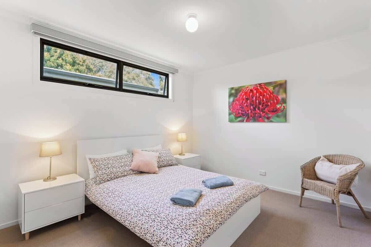 Quarto com uma cama, duas mesas de cabeceira com abajures, uma cadeira, uma janela e um quadro na parede.