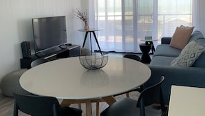 Ein modernes Wohnzimmer mit einem runden Esstisch, schwarzen Stühlen, einer Couch und einem Fernseher.