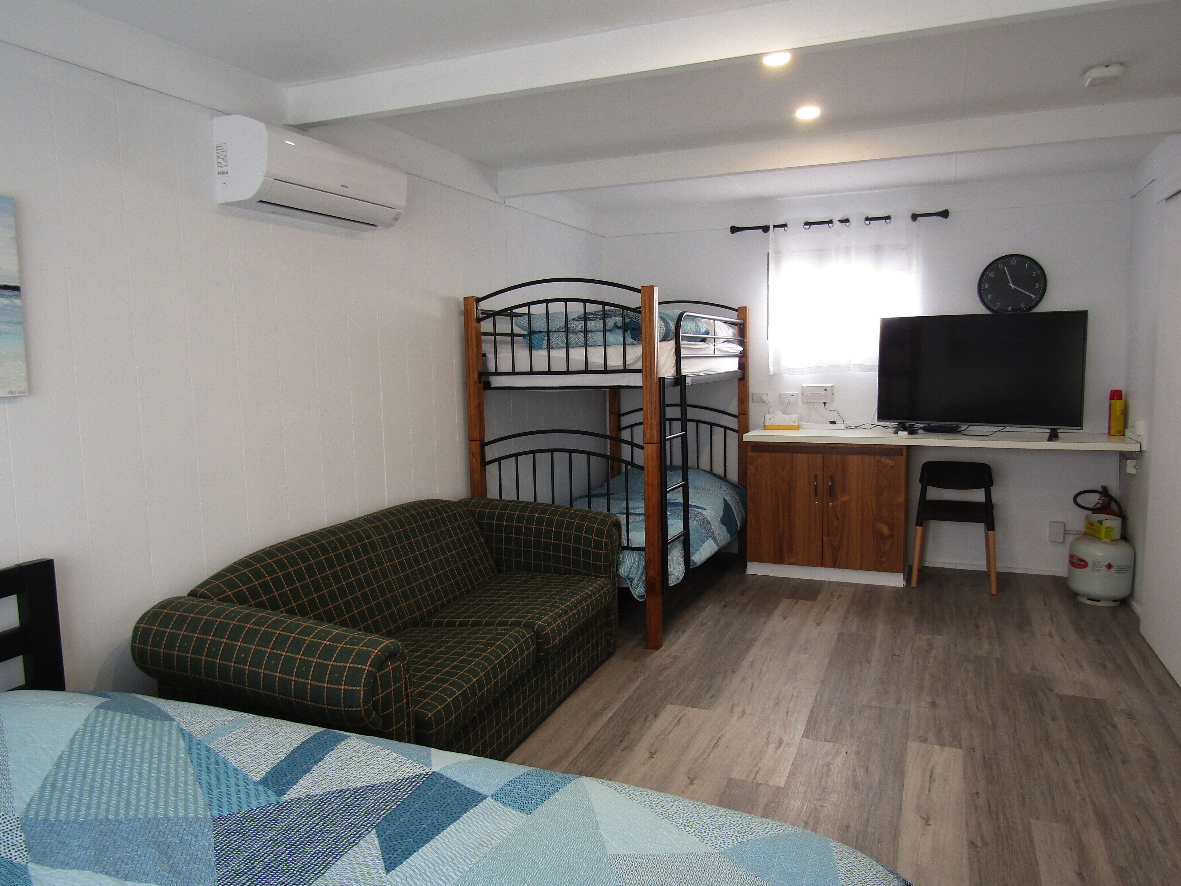 Een kleine kamer met stapelbedden, een slaapbank, een bureau met een televisie en een stoel.