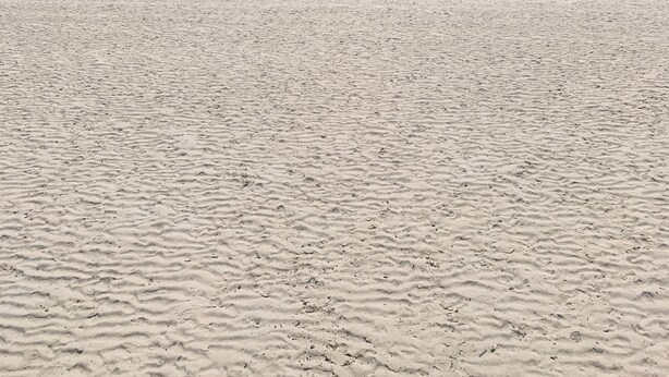 Ein Sandstrand mit blauem, wolkenlosem Himmel.