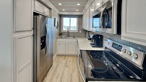 A modern kitchen with white cabinetry, stainless steel appliances, and a black stove. - Regency Towers #812 | Comp. Beach Service, Beautiful Views + Amenities (Panama City Beach)