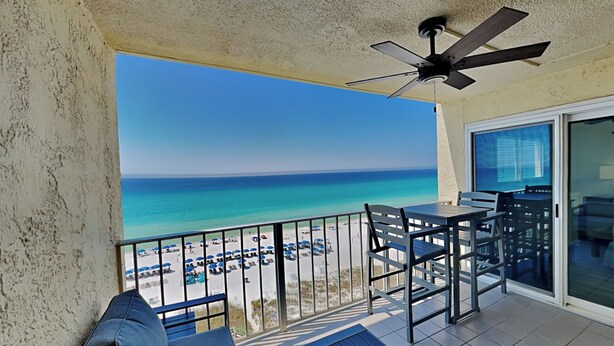 A balcony with a view of the beach, a ceiling fan, and a table with chairs. - Regency Towers #812 | Comp. Beach Service, Beautiful Views + Amenities (Panama City Beach)