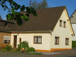Ein zweistöckiges Haus mit braunen Ziegeln auf dem Dach, einer Haustür und zwei Fenstern im Erdgeschoss.