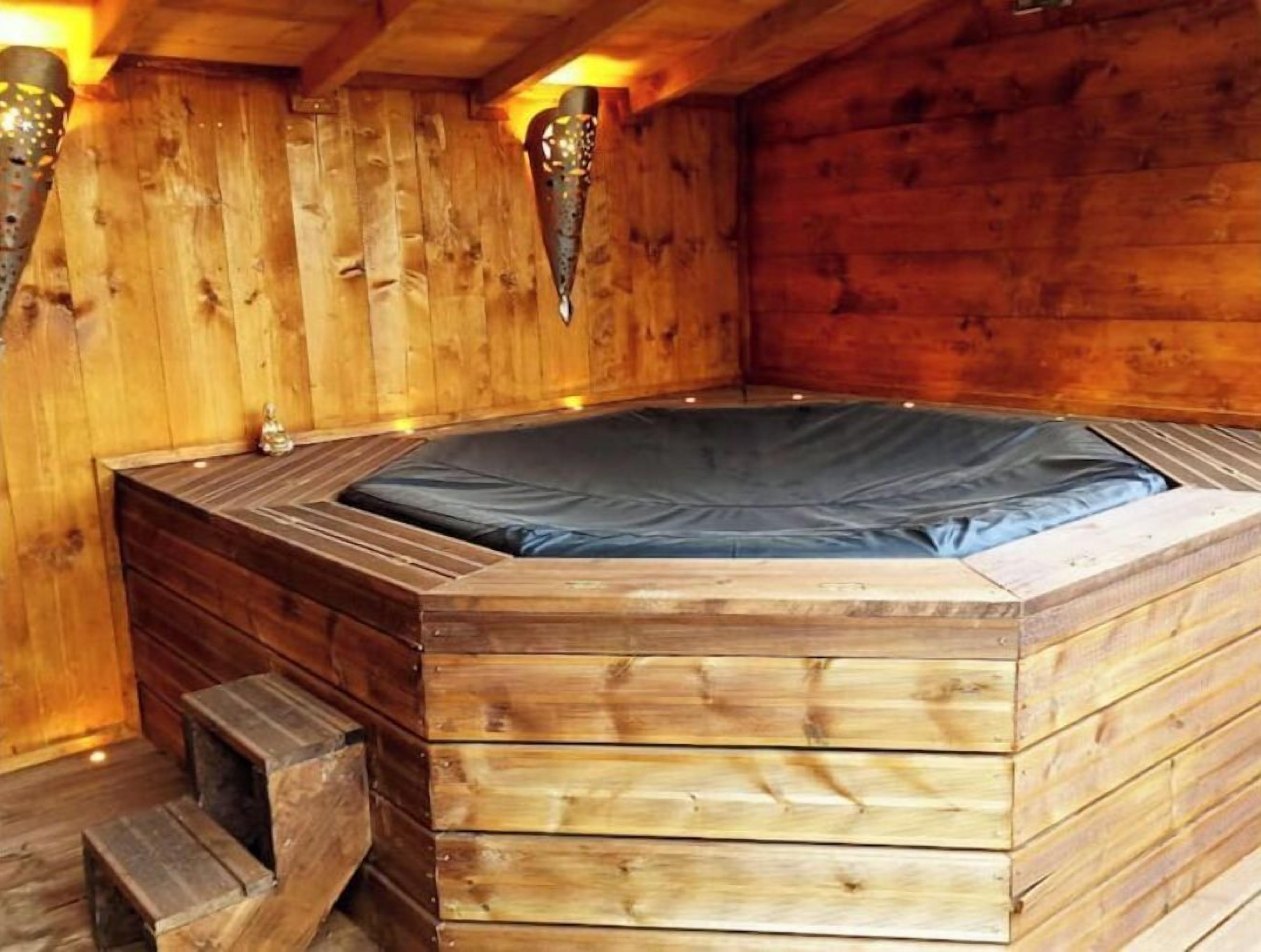 Een houten kuip met een zwarte deksel, houten traptreden ernaartoe en wandlampen.