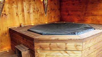 Een houten kuip met een zwarte deksel, houten traptreden ernaartoe en wandlampen.