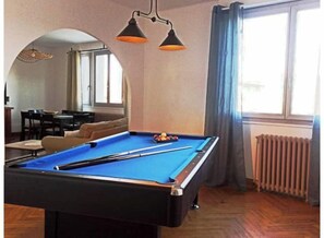 A pool table in a room with a dining area, large windows, and a radiator.
