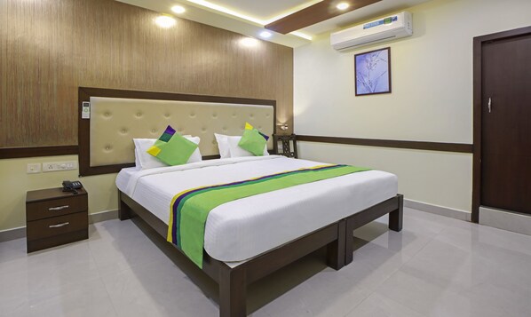 Una habitación de hotel con cama, mesita de noche y aire acondicionado instalado en la pared.