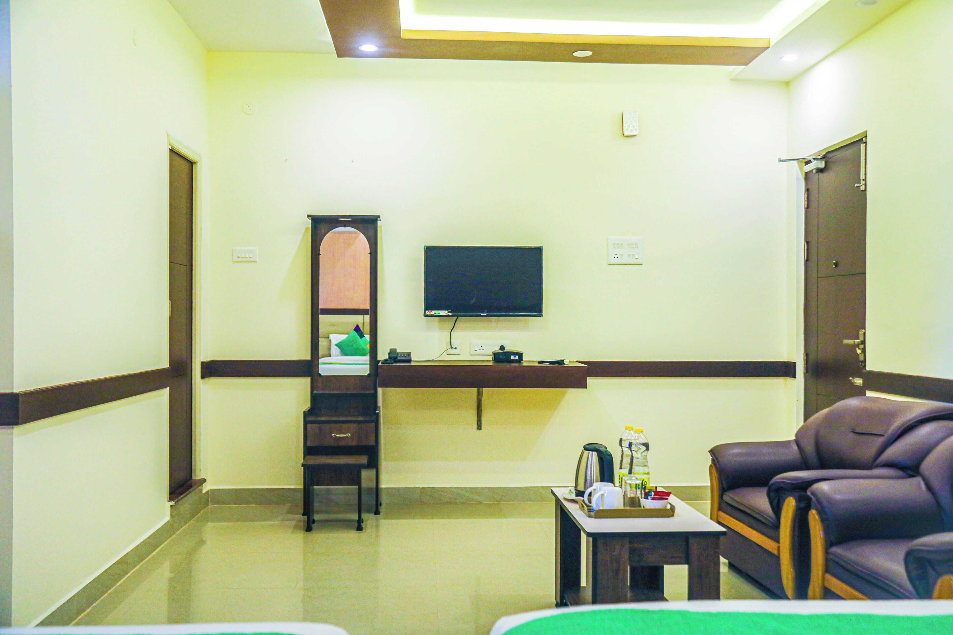A hotel room with a flat-screen TV mounted on the wall, a wooden cabinet, a sofa, and a small table with a tray.