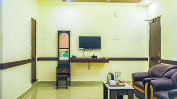 A hotel room with a flat-screen TV mounted on the wall, a wooden cabinet, a sofa, and a small table with a tray.