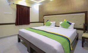 Habitación de hotel con cama, cabecero de madera, mesita de noche y cortina roja.