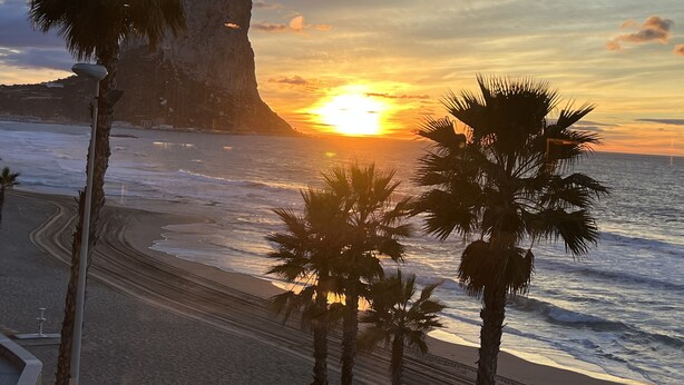 A sunset over a beach with palm trees and a rocky cliff. - Chic bungalow in a quiet and central location with private pool - close to the beach (Calpe)