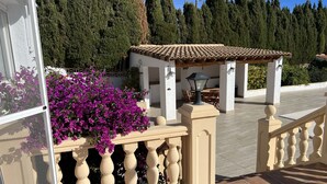 A covered outdoor seating area with a tiled roof, surrounded by a beige balustrade and a potted plant with purple flowers. - Chic bungalow in a quiet and central location with private pool - close to the beach (Calpe)