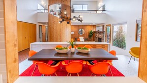 Un espace repas moderne avec une table en bois foncé, des chaises orange vif et un tapis rouge.