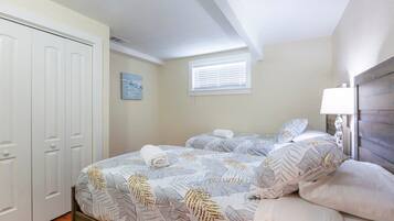 A bedroom with two beds, a white wardrobe, a window with blinds, and a wall-mounted lamp.