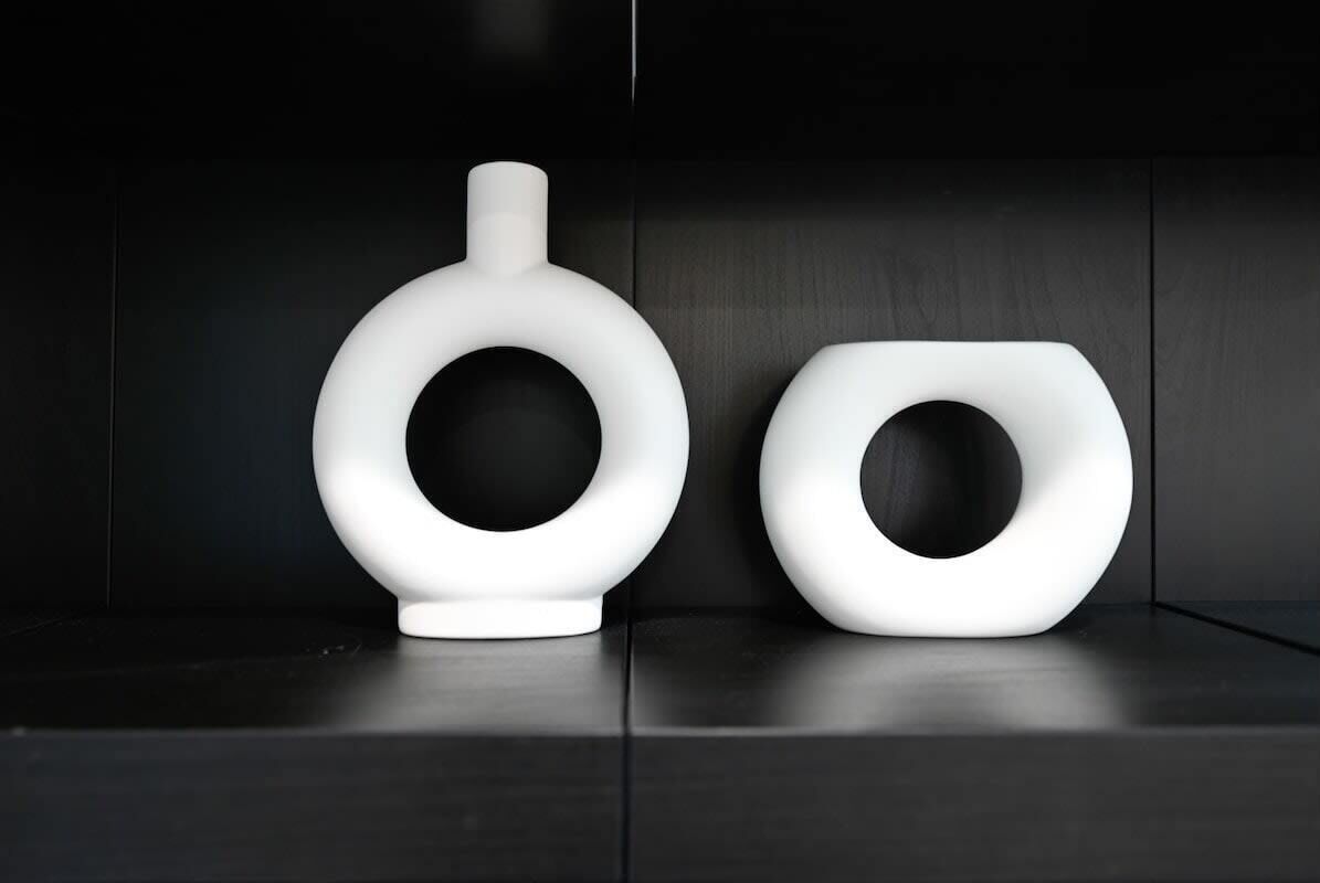 Deux objets circulaires blancs et modernes, dotés d’un trou central, sont posés sur une surface en bois sombre.