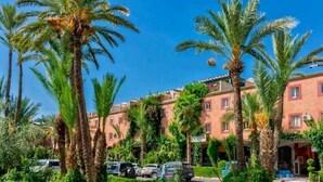 Un hôtel à plusieurs étages, bordé de palmiers et avec des voitures garées devant.