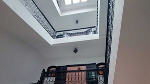 Un intérieur à plusieurs niveaux, doté d’une verrière, d’un escalier, d’un coin repas avec des chaises et d’une cuisine visible à travers une porte ouverte.
