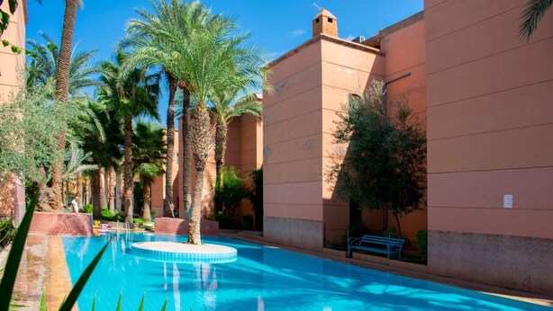 Une piscine entourée de palmiers et de bâtiments de couleur beige.