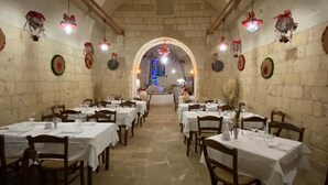 A restaurant with stone walls, white tablecloths, and hanging decorations. Tables are set with glasses and cutlery. - Masseria Antoglia (Villa Castelli)