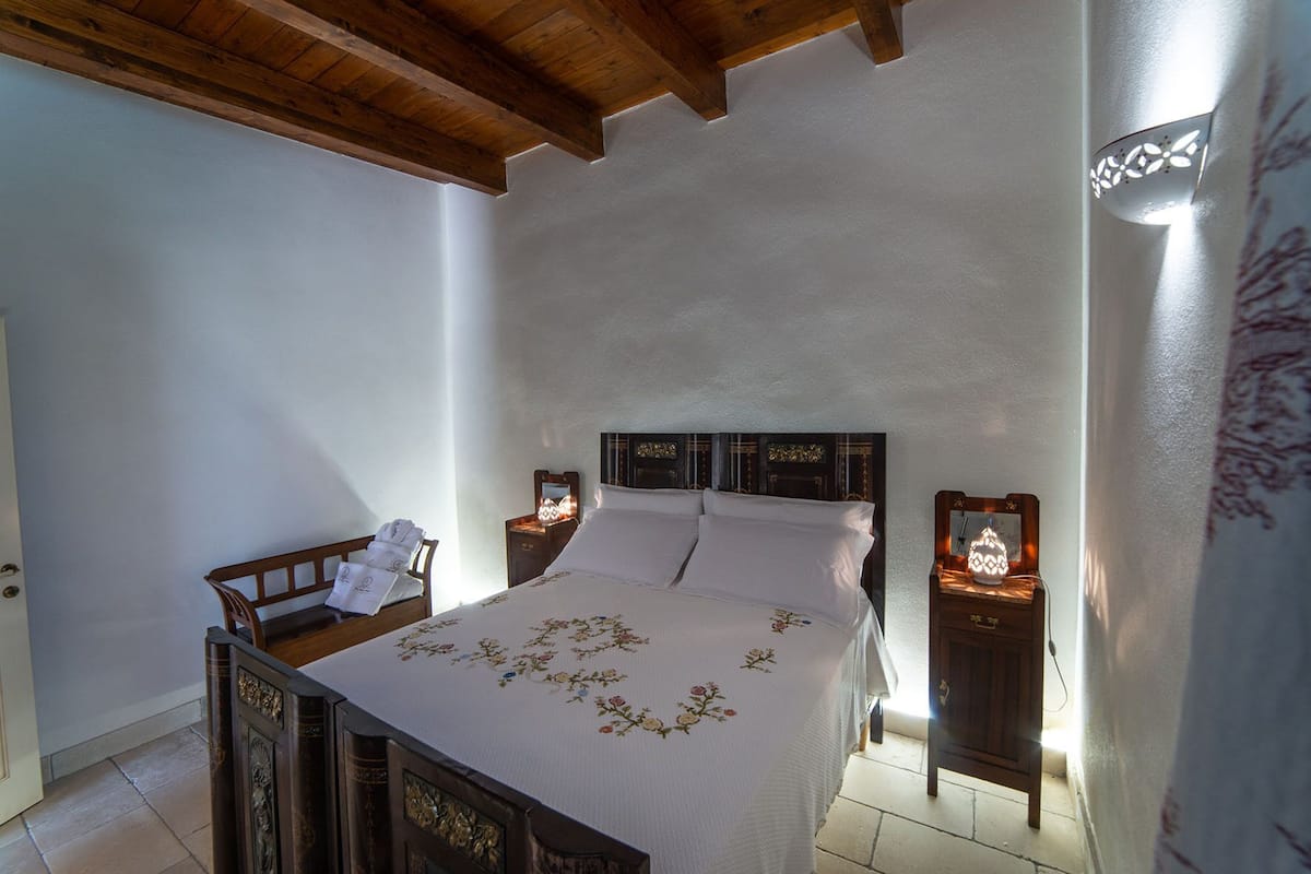 Un dormitorio con una cama de madera, ropa de cama blanca y dos mesitas de noche con lámparas.
