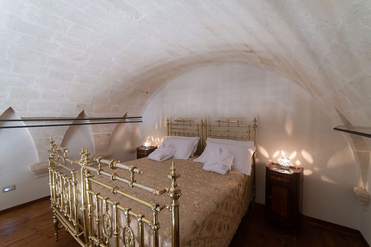 Un dormitorio con techo abovedado, cama con cabecera de metal ornamentada y dos mesitas de noche con lámparas.
