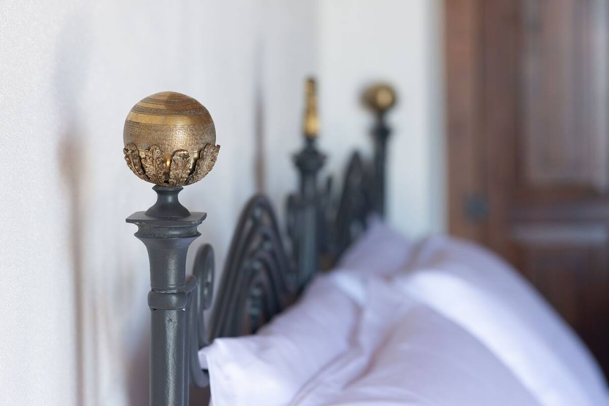 Una cama con cabecera adornada con un remate decorativo y una barra de metal.