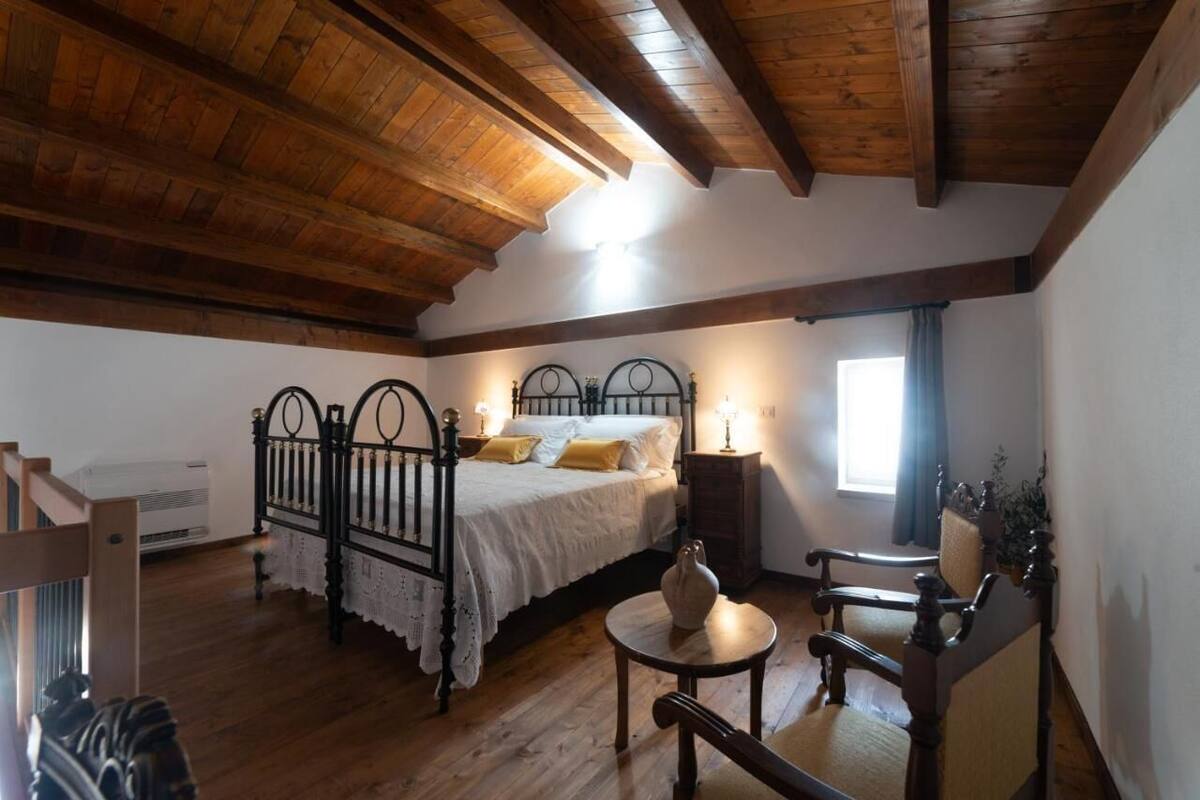 Un dormitorio con techo de madera, una cama con sábanas blancas, una mesita de noche con una lámpara y una silla.