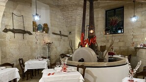 A rustic dining area with stone walls, wooden tables, and a central stone fireplace. - Masseria Antoglia (Villa Castelli)