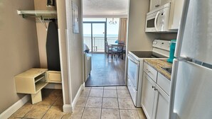 A narrow kitchen with a microwave, refrigerator, and a small dining area with a view of the ocean.
