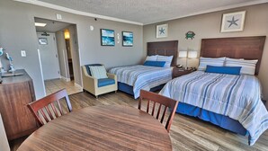 A hotel room with two beds, a dining table, and a chair. There are framed pictures on the wall and a star decoration above the beds.