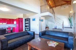 A spacious living area with two black leather sofas, a wooden coffee table, and a red kitchen in the background. - Villa Rigani - Three Bedroom Villa, Sleeps 6 (Lefkada)