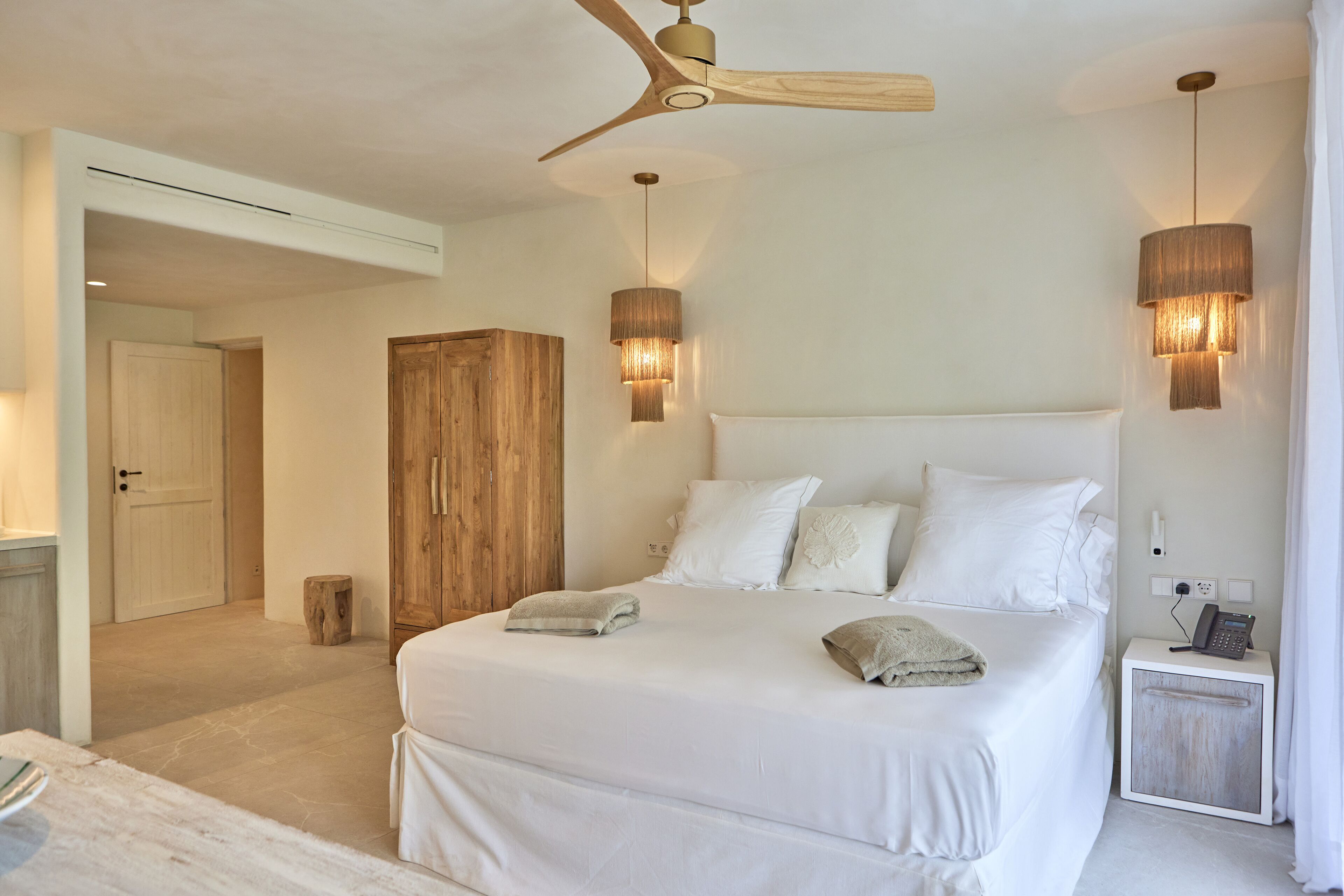 A bedroom with a large bed, wooden wardrobe, bedside lamps, and a ceiling fan.