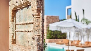 A rustic door with intricate carvings, leading to a pool area with lounge chairs and umbrellas. - Mar Suites Formentera by Universal Beach Hotels (Formentera)