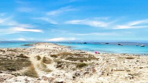 Una playa con aguas azules cristalinas, embarcaciones y vegetación escasa.