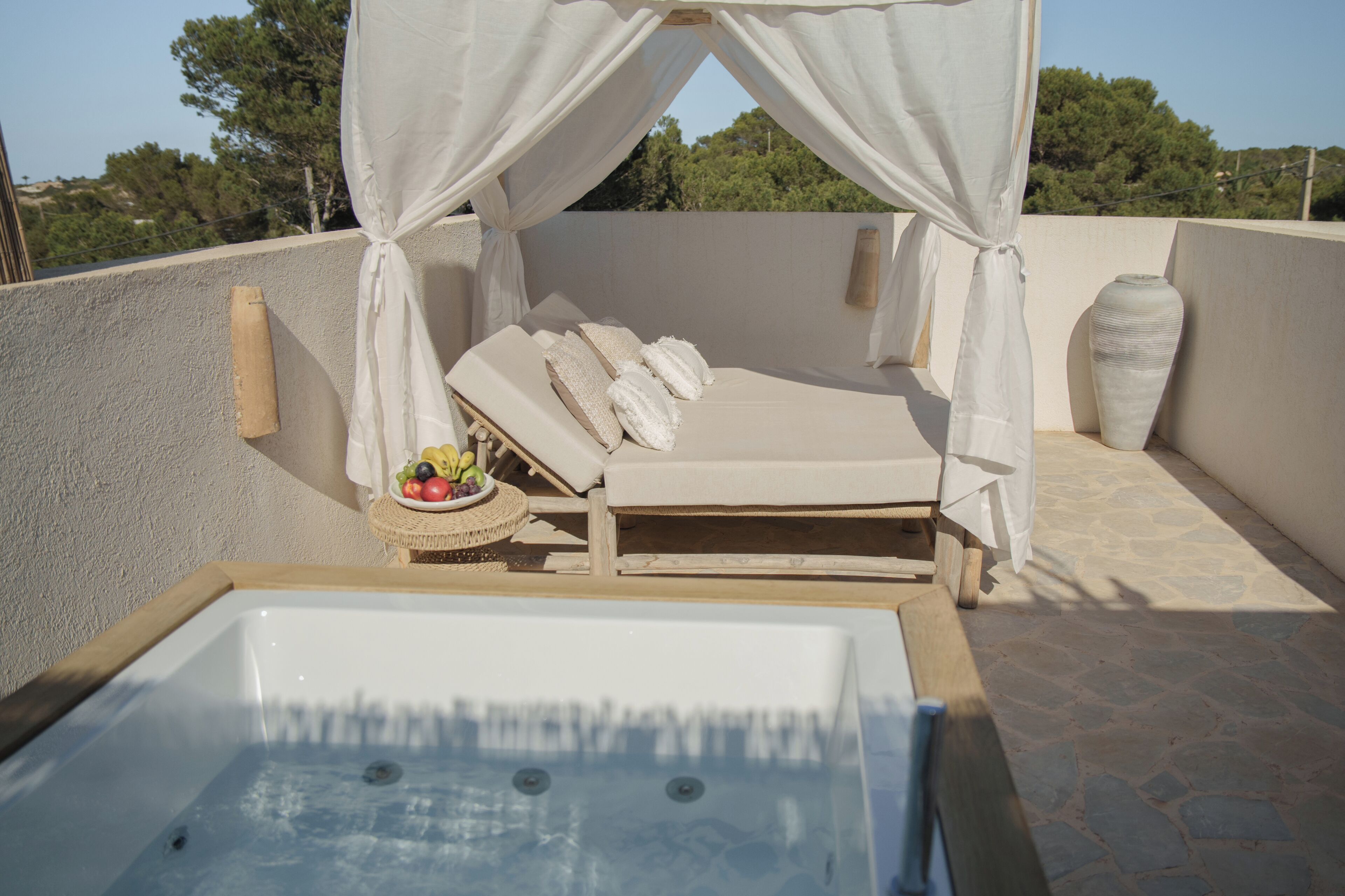 A sunbed with a canopy, a hot tub, and a fruit bowl on a rooftop terrace.
