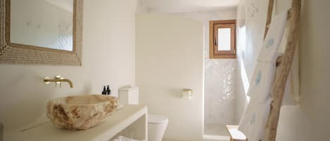 A bathroom with a stone sink, a wooden bench, a wooden ladder, and a window.