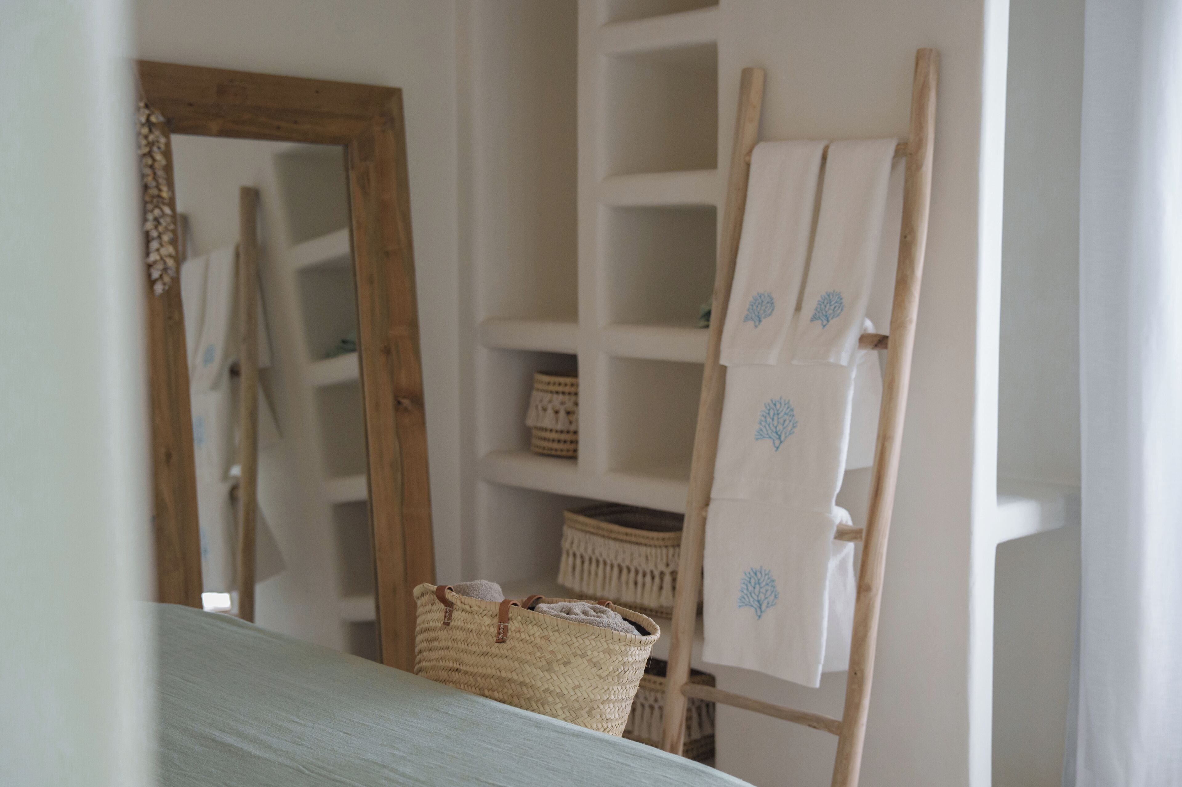 Una habitación con una escalera de madera apoyada en una pared, una cesta tejida sobre una mesa y estantes con cestas y telas dobladas.