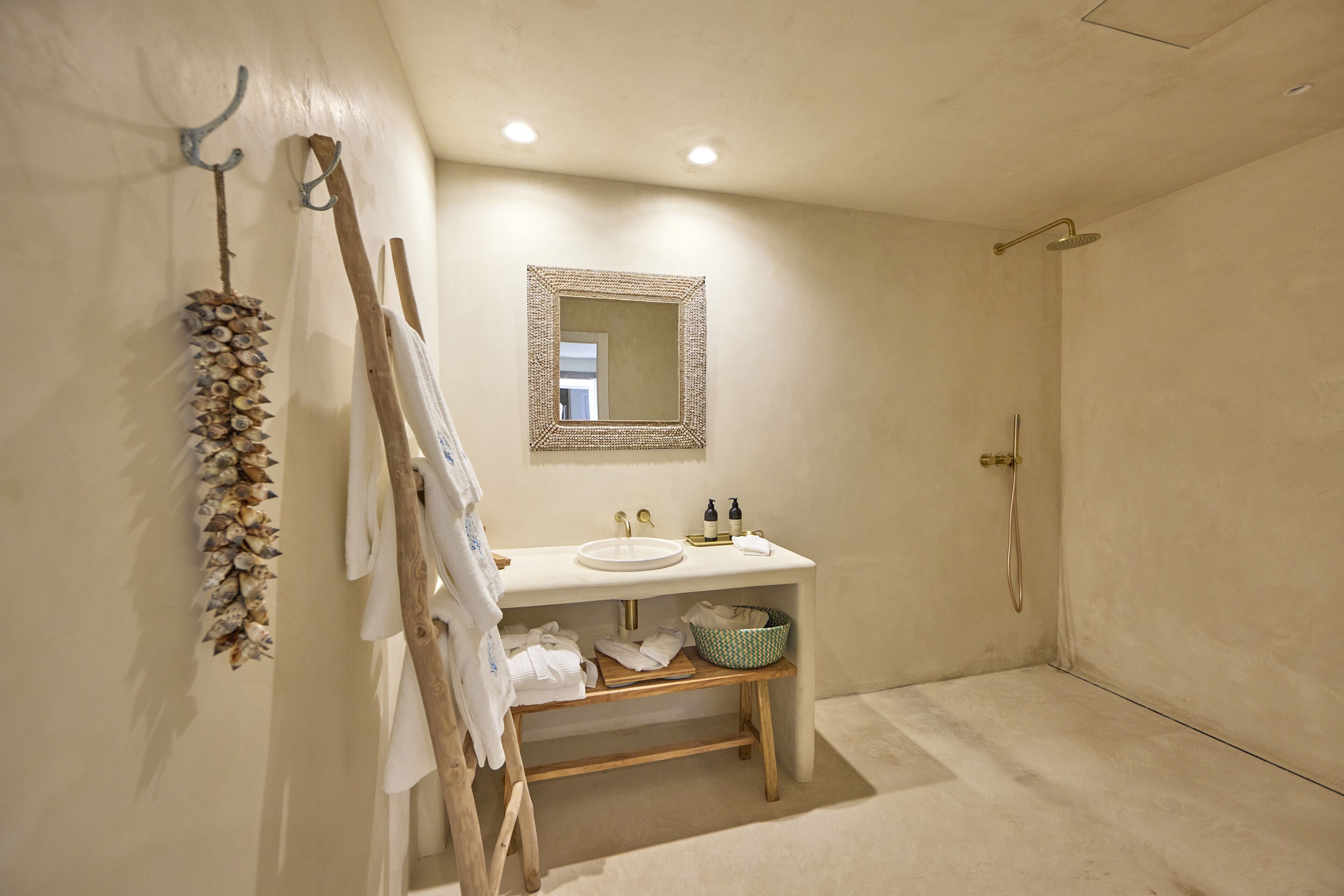 A bathroom with a sink, mirror, shower, and wooden bench.