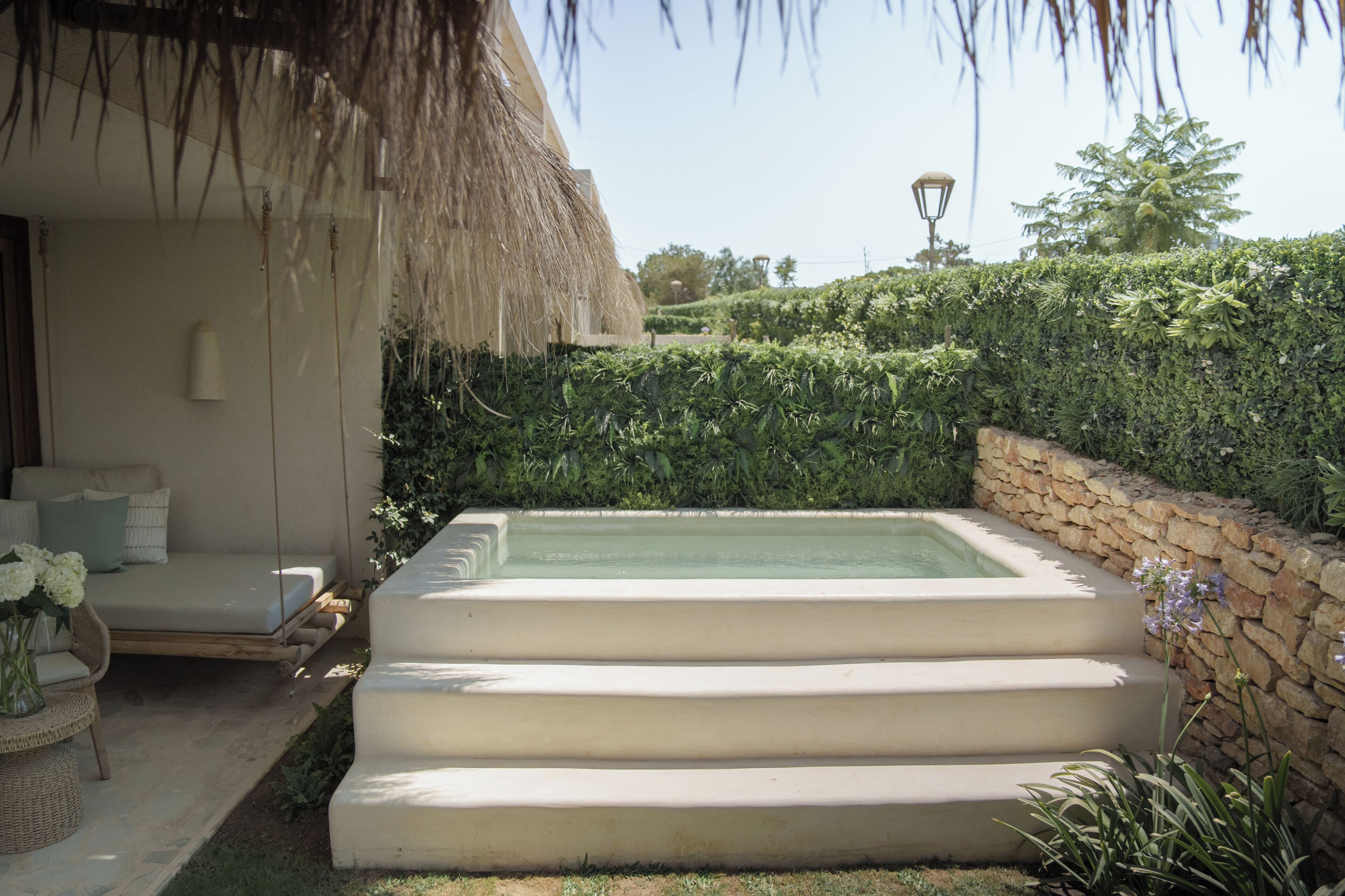 A pool with steps leading into it, surrounded by a stone wall and lush greenery.