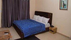 A bedroom with a bed, a nightstand, a remote control, and a curtain. - Go2Hotel45 (Lagos)