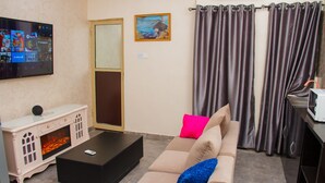 A living room with a flat-screen TV, a fireplace, a sofa with colorful cushions, and a curtain. - Go2Hotel45 (Lagos)