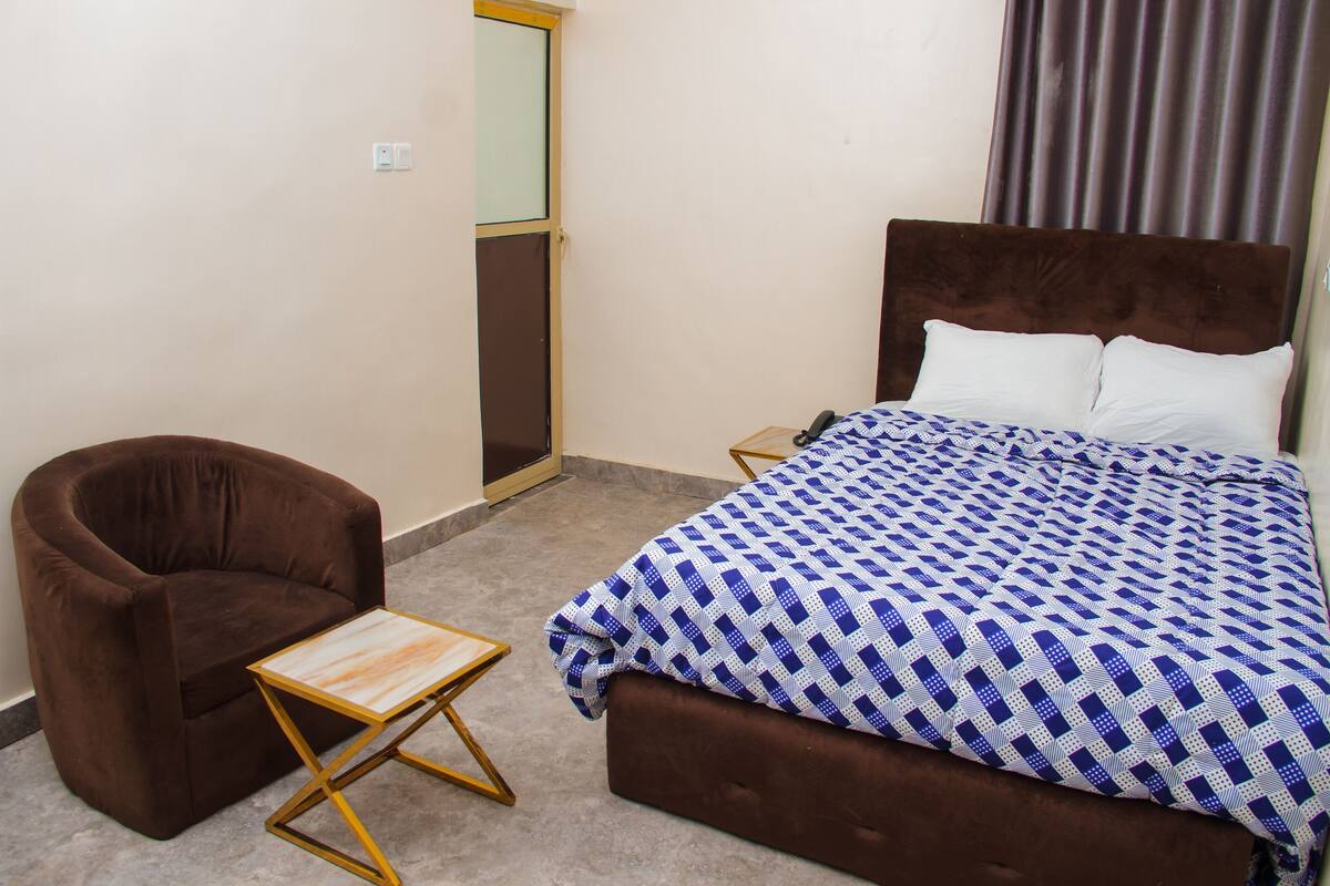 A bedroom with a bed, a chair, a small table, and a mirror.