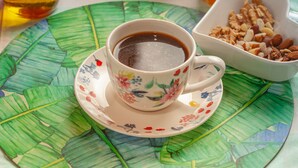 Aamiaispöydällä on monenlaisia hedelmiä, lasi appelsiinimehua, pullo öljyä, kuppi kahvia ja kulho pähkinöitä.