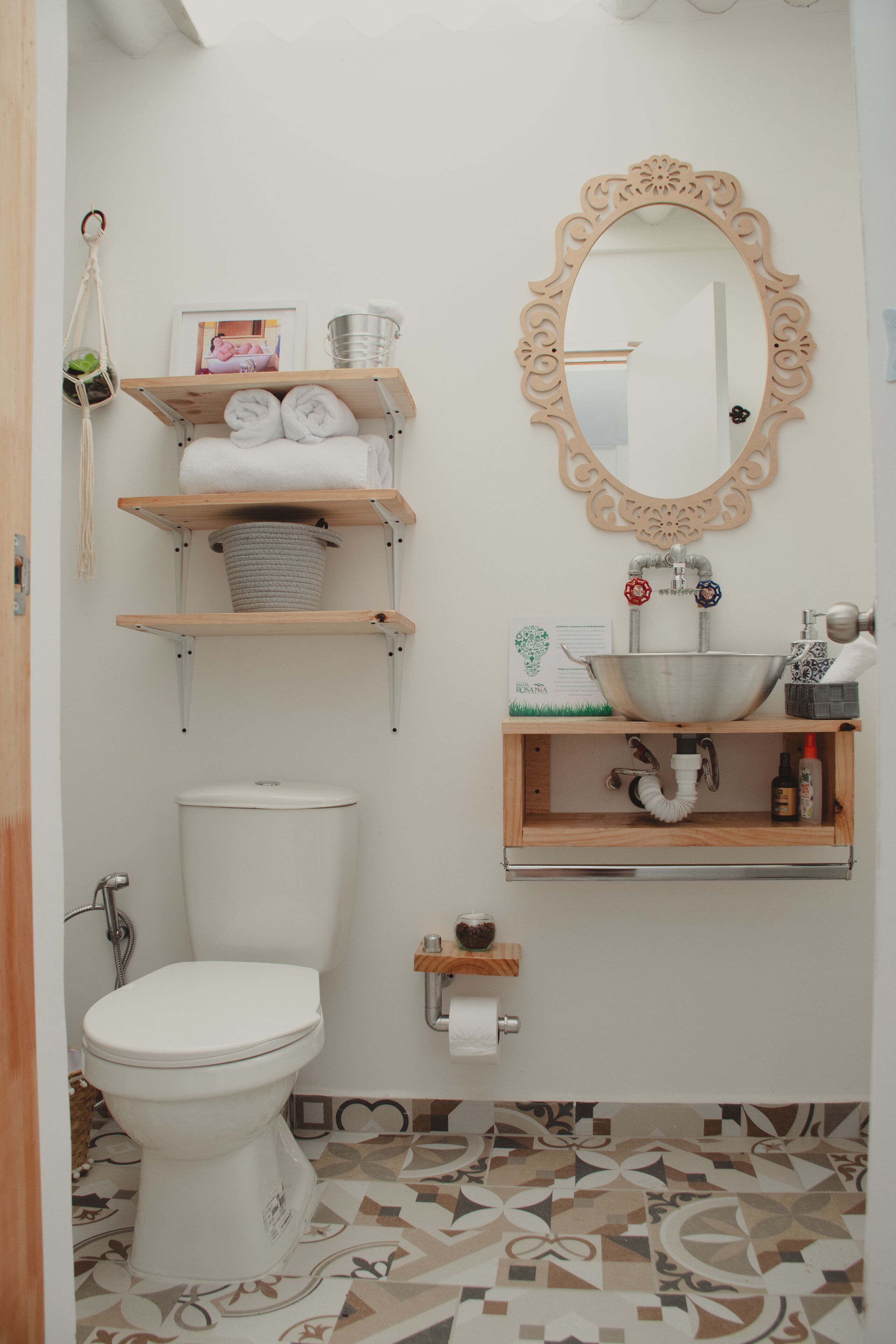 A bathroom with a toilet, a sink with a decorative mirror, and shelves with towels and toiletries.