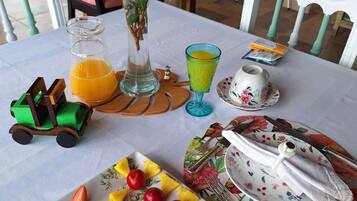 A breakfast table with fruit, a vase with flowers, a glass of orange juice, and a toy car.