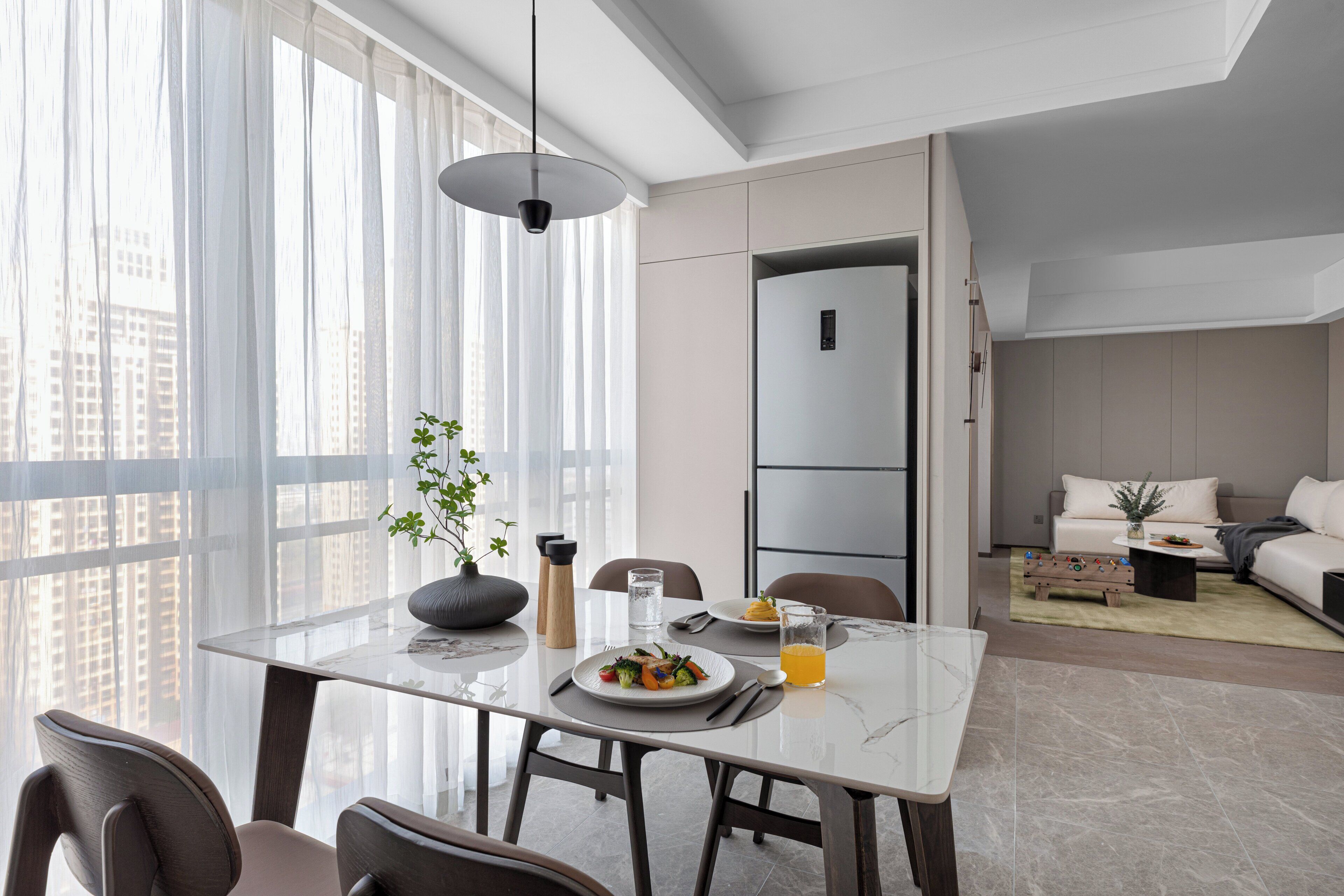 A modern dining area with a marble table, chairs, and a view of the city through large windows.