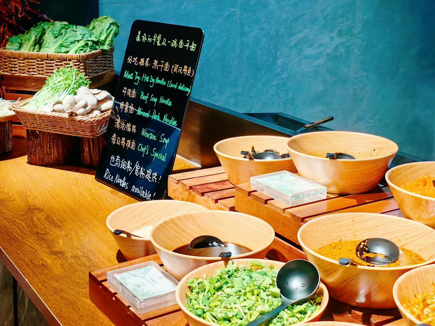 A buffet table with various dishes and a signboard with menu items in a foreign language.