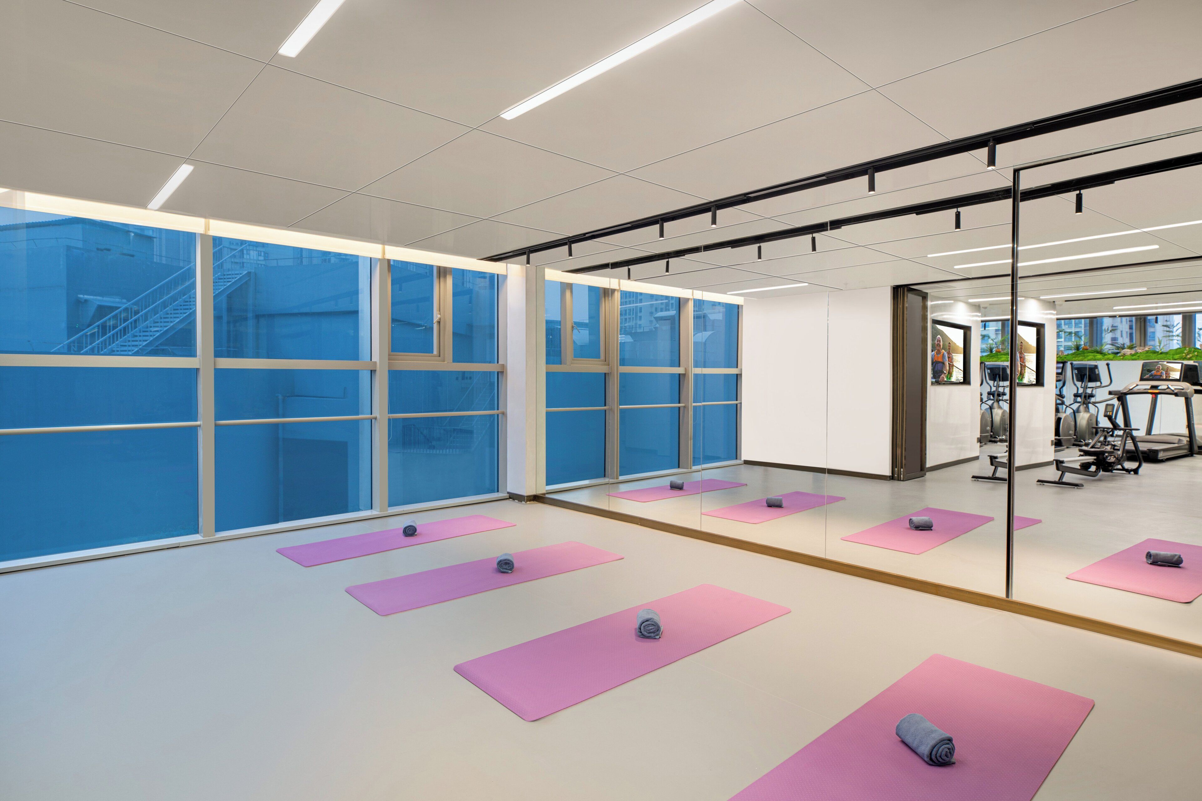 A spacious room with large windows, exercise mats, and gym equipment.