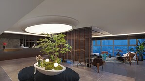 Un vestíbulo moderno con un macetero circular central, zona de estar y grandes ventanales con vistas a la ciudad.