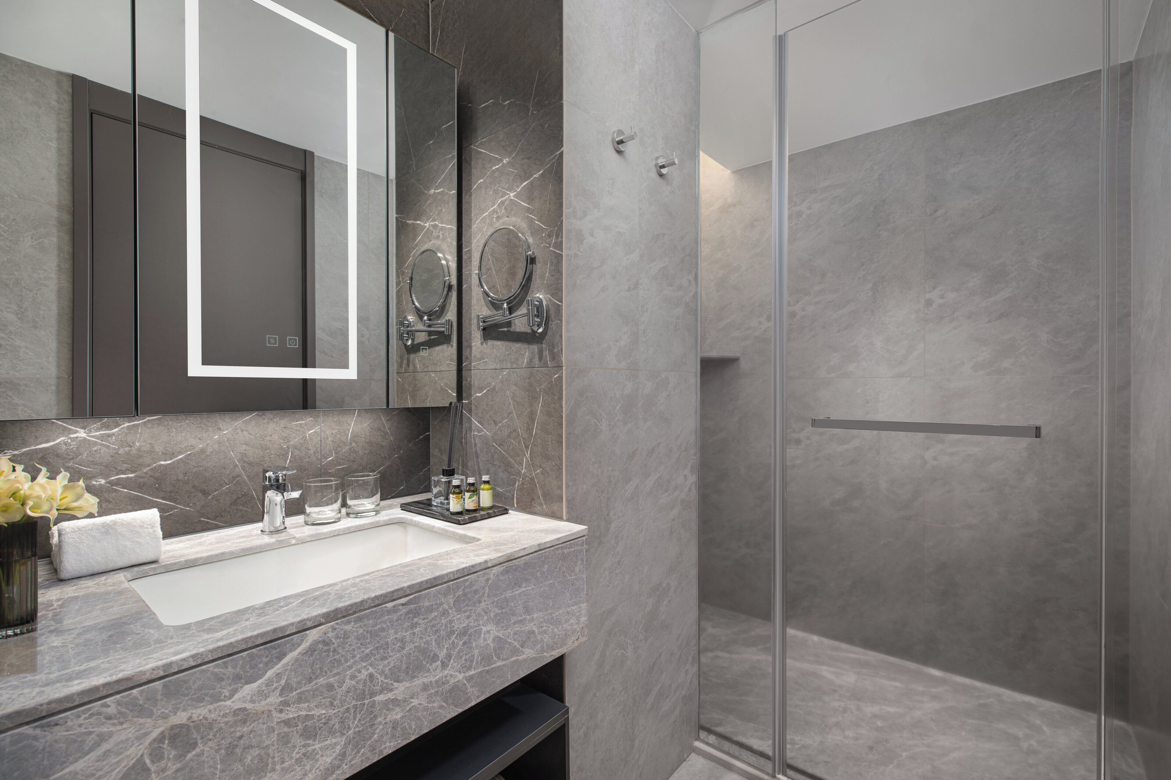 Un baño moderno con lavamanos de mármol, un espejo grande y una ducha con mampara de vidrio.